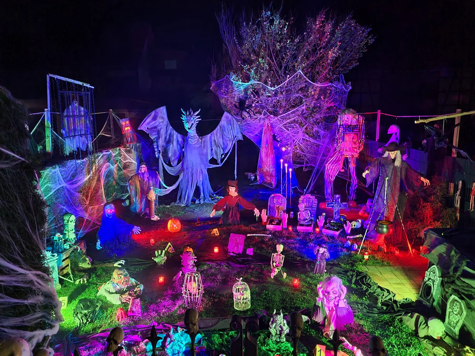 Der Halloween Garten bei Nacht: beleuchtete Figuren, Spinnweben und ein riesiger Drache zwischen den Bäumen